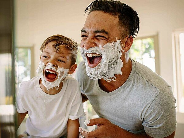 Vater mit Sohn vor dem Badezimmerspiegel mit Rasierschaum im Gesicht